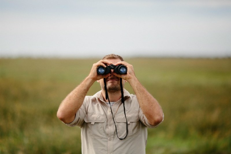 homme qui regarde à travers une paire de jumelles dans la nature